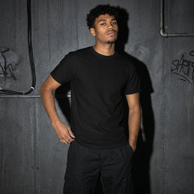 Schwarzes Art of Techno T-Shirt am Model, Vorderansicht vor Betonwand